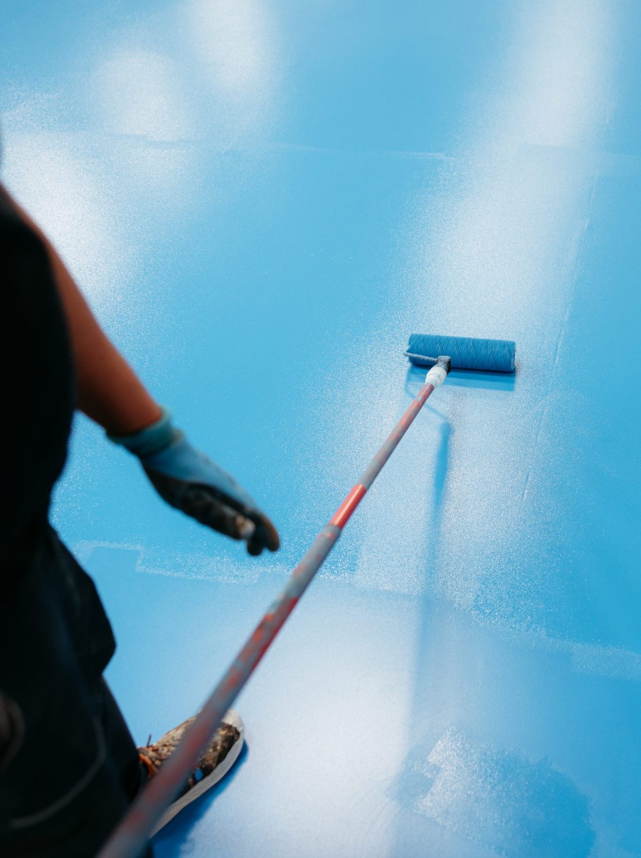 Construction worker applying blue epoxy resin on rubber flooring using a roller